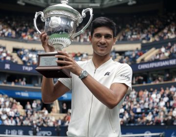 1. Carlos Alcaraz holds a trophy triumphantly in front of a cheering crowd after winning the China Open tennis championship. 2. Celebrating his victory, Carlos Alcaraz raises a trophy before an enthusiastic crowd following his win at the China Open. 3. In front of a lively audience, Carlos Alcaraz proudly displays his trophy after clinching the title at the China Open.