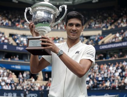 1. Carlos Alcaraz holds a trophy triumphantly in front of a cheering crowd after winning the China Open tennis championship. 2. Celebrating his victory, Carlos Alcaraz raises a trophy before an enthusiastic crowd following his win at the China Open. 3. In front of a lively audience, Carlos Alcaraz proudly displays his trophy after clinching the title at the China Open.